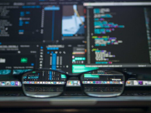 Unas gafas delante de una pantalla de ordenador que muestra código.